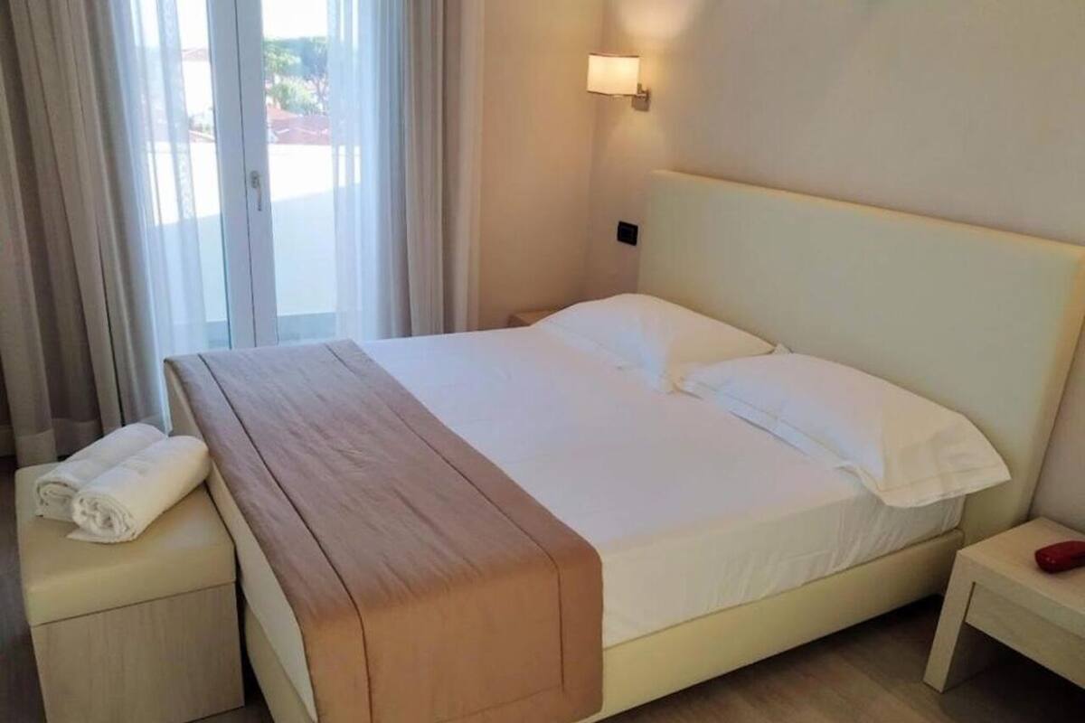 Ein Hotelzimmer mit einem großen Bett, einem Nachttisch, einem kleinen Beistelltisch und einem Fenster mit Vorhängen.