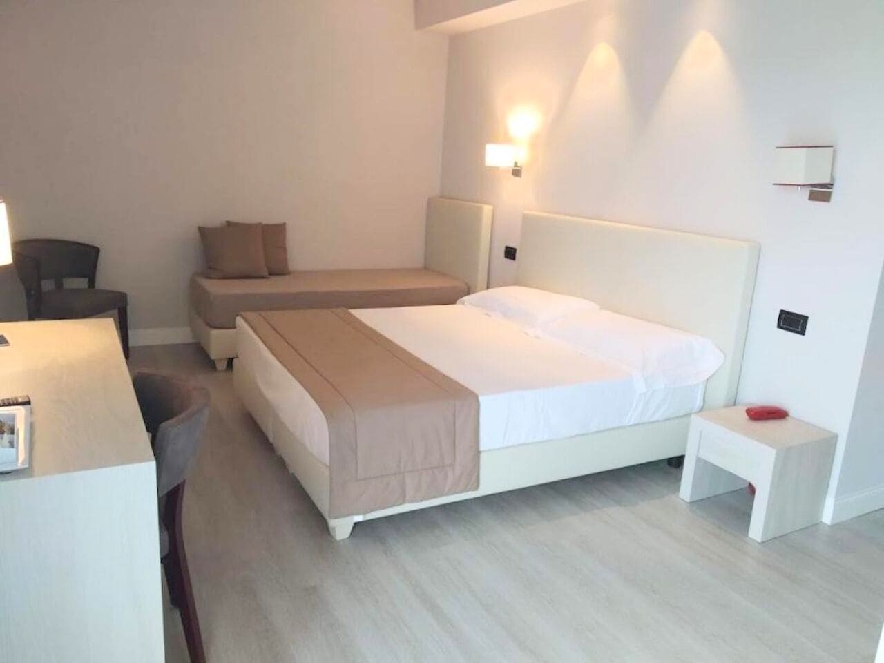 A hotel room with a large bed, a smaller bed, a desk, and a chair.