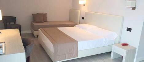 A hotel room with a large bed, a smaller bed, a desk, and a chair.