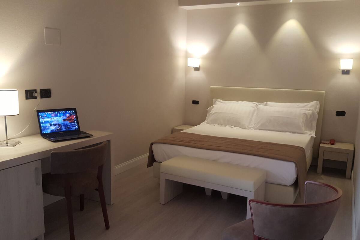 Ein Hotelzimmer mit Bett, Nachttischen, einem Schreibtisch mit Laptop, einem Sessel und einer Lampe.