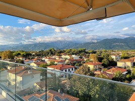 Un balcón con vistas a una zona residencial, casas con tejados rojos y montañas al fondo.