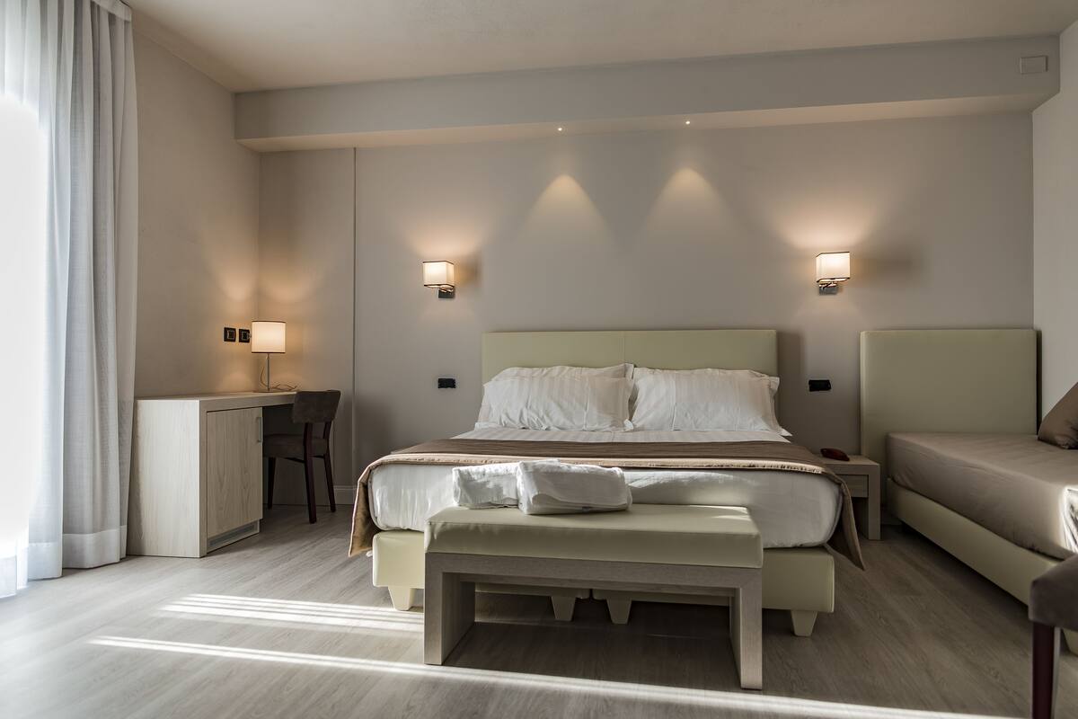 Ein Hotelzimmer mit einem großen Bett, einem Schreibtisch, einer Bank und zwei Nachttischen mit Lampen.