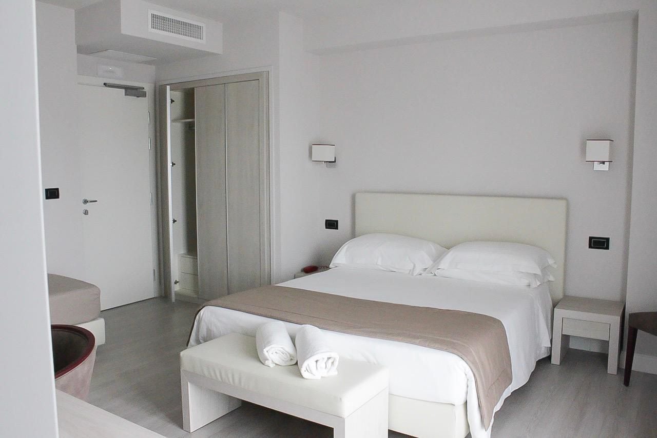 Una habitación de hotel moderna con una cama grande, mesitas de noche, un banco y un armario.