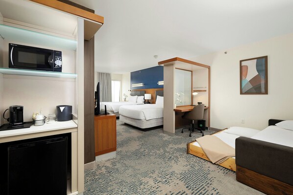 A hotel room with a kitchenette, a bed, a desk, and a bathroom.