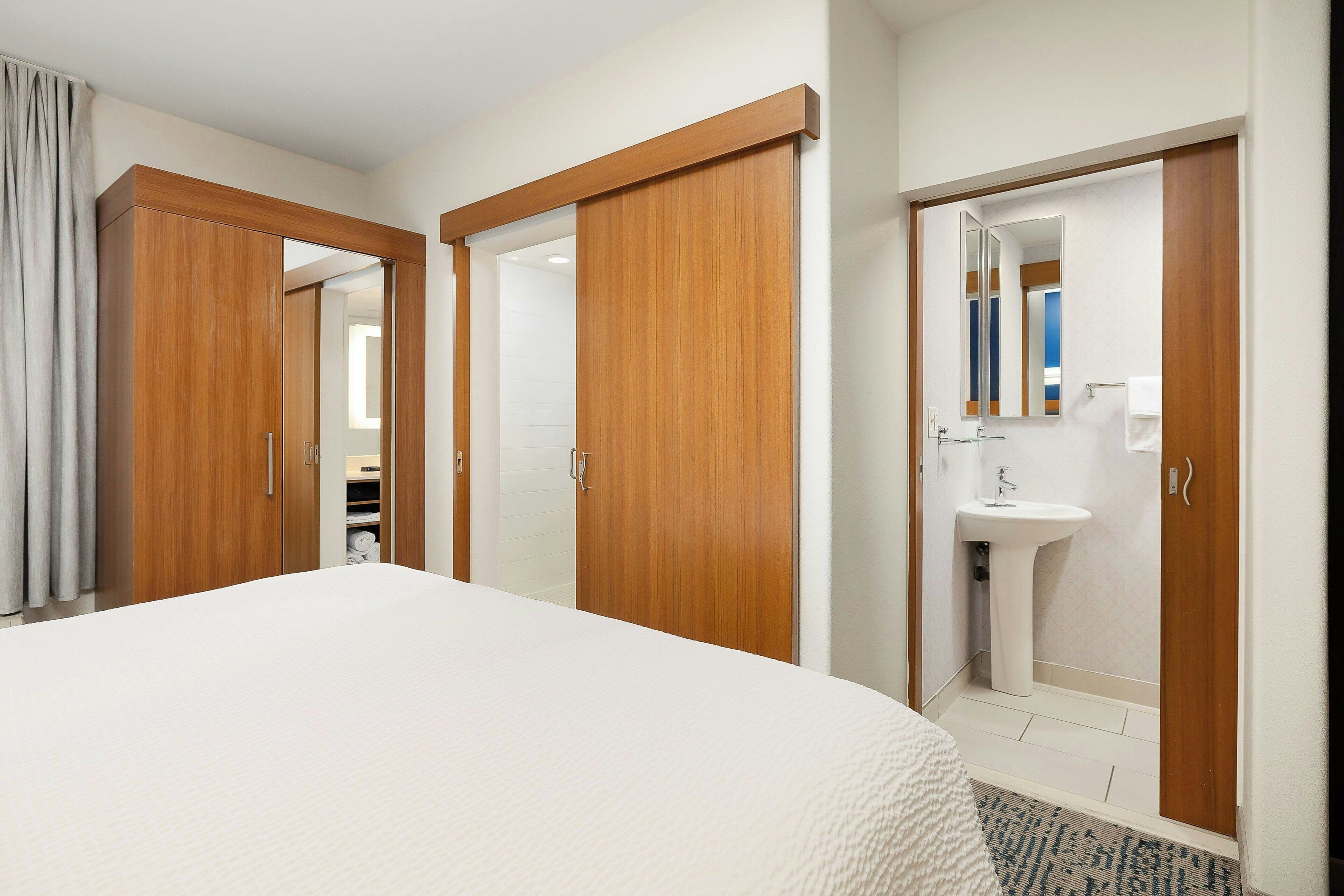 A hotel room with a large bed, wooden wardrobe, and a bathroom with a sink and mirror.