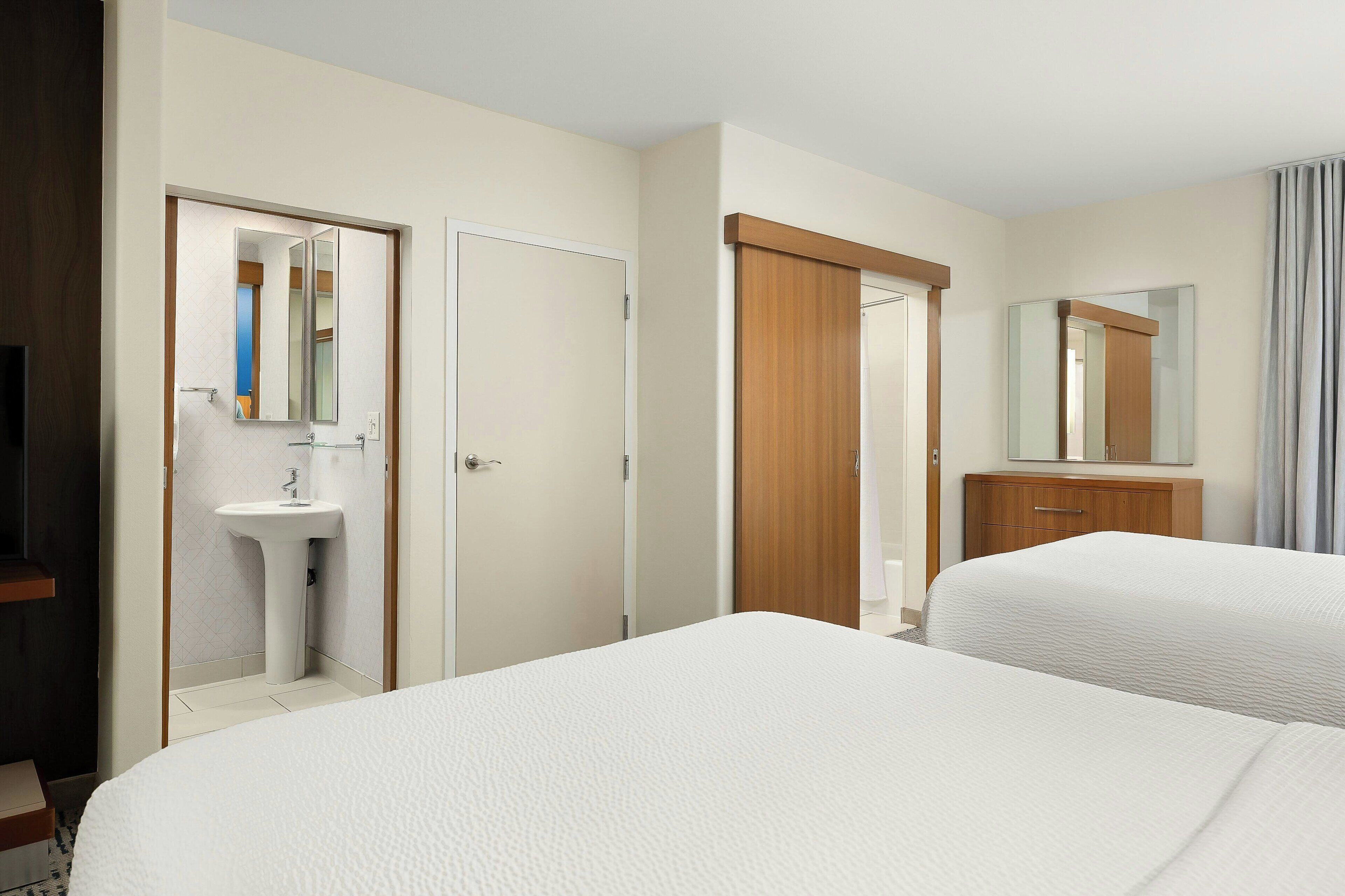 A hotel room with two beds, a wooden wardrobe, a white sink, and a mirror.