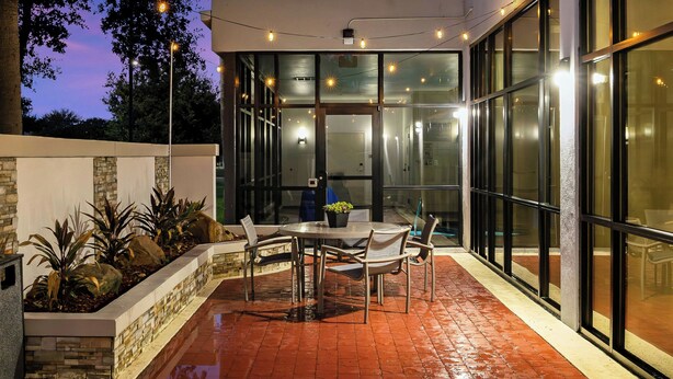An outdoor patio with a table and chairs, surrounded by glass walls and a stone planter with plants. - SpringHill Suites by Marriott McAllen Convention Center (McAllen)