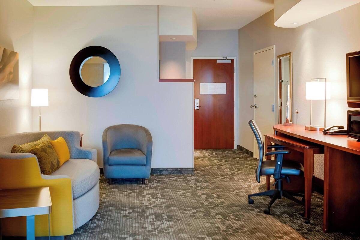 Ein Hotelzimmer mit einer Couch, einem Sessel, einem Schreibtisch und einem Spiegel an der Wand.