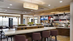 Un espace bar moderne doté d’un îlot central, de tabourets de bar et d’un présentoir pour la carte des boissons et des plats.