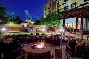 An outdoor patio with a fire pit, seating, and a building in the background.