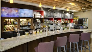 Un espace bar doté d’un long comptoir, de nombreux tabourets et d’un tableau affichant le menu.