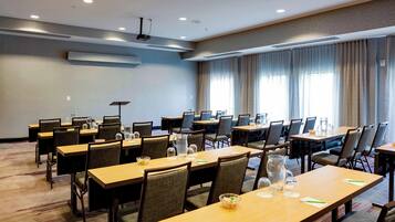 Une salle de conférence dotée de plusieurs tables et chaises, équipée de carafes et de verres d’eau, et de grandes fenêtres avec des rideaux.