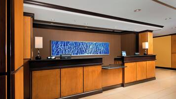 A hotel reception area with a wooden reception desk, a large blue abstract artwork on the wall, and a modern ceiling design.