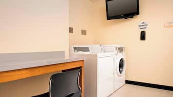A laundry room with a washing machine, dryer, and a desk with a chair. There is a television mounted on the wall and a sign indicating the room is for employees only.
