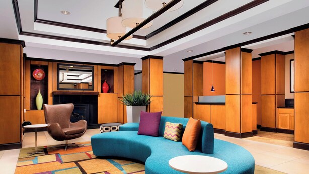 A modern living area with a curved blue sofa, a small round table, and a brown armchair. There is a fireplace with a mirror above it and a potted plant on the floor.