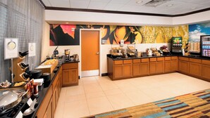 A hotel kitchen with a buffet setup, including a coffee station, a refrigerator, and a microwave.