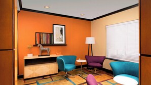 A room with two blue armchairs, a purple armchair, a small white table, a lamp, and a framed picture on the wall.