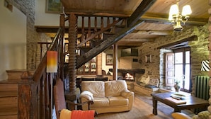 A rustic interior with a stone wall, wooden staircase, leather sofa, and a fireplace.