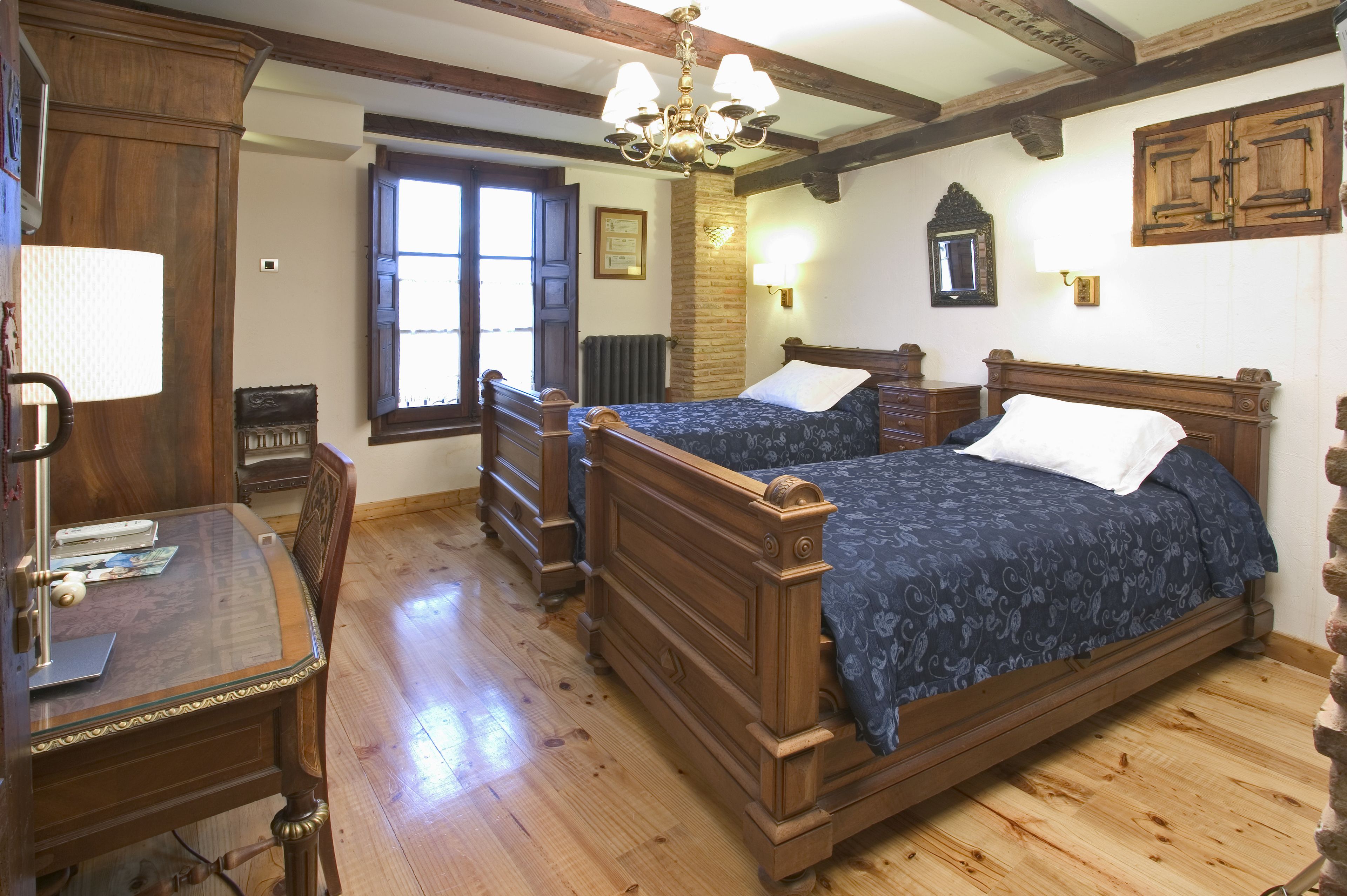 Una habitación tradicional con dos camas de madera, un escritorio con lámpara y una ventana con vistas.
