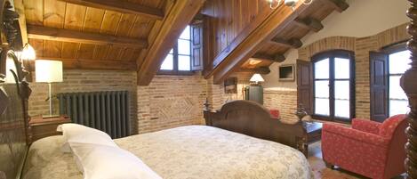 A traditional room with a large bed, a red armchair, wooden beams, and a brick wall.