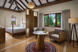 A hotel room with a bed, a round table with two glasses and a plate of food, a chair, a lamp, and a window with curtains. - Mercure Goa Devaaya Resort (Panaji)