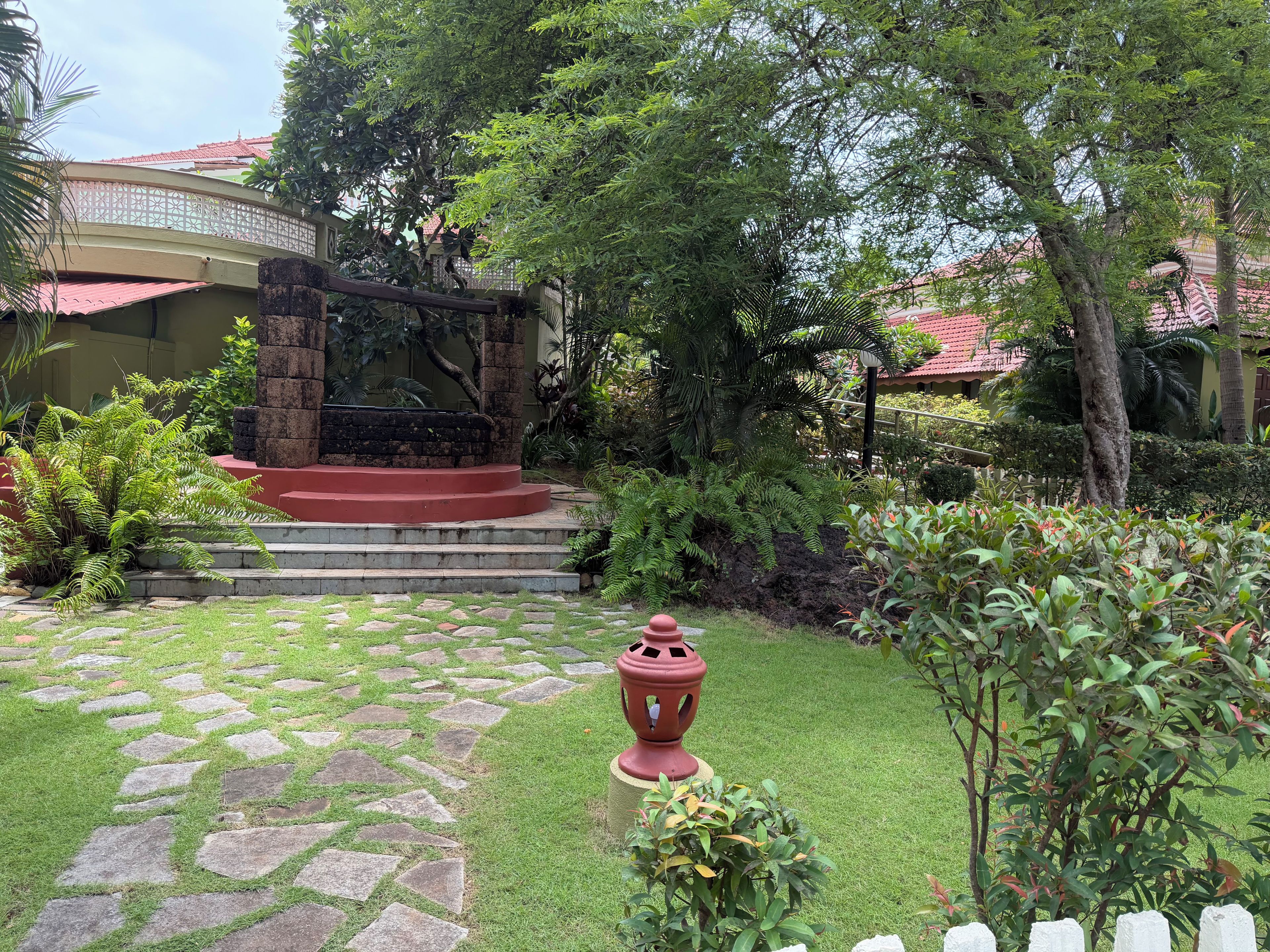 A garden with a stone pathway, a red lantern, and a stone staircase leading to a building with a red roof.