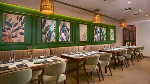 A restaurant with booths, tables, and chairs, with artwork on the walls and pendant lighting. - Mercure Goa Devaaya Resort - An Accor Hotels Brand (Panaji)