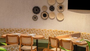 A restaurant with round tables, wicker chairs, and a variety of woven wall decorations.