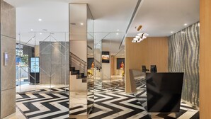 A modern lobby with a geometric patterned floor, a staircase, and a reception desk.