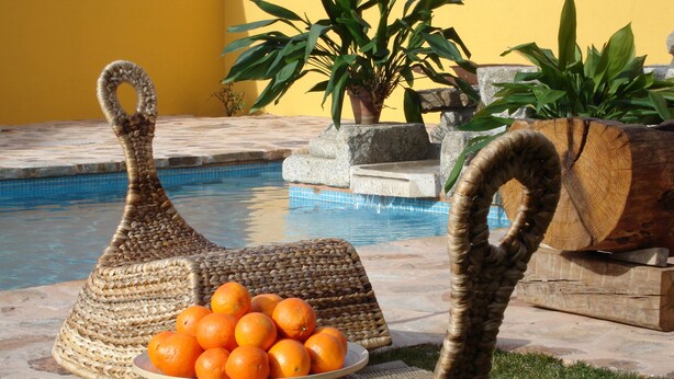 Wicker chairs with a plate of oranges, a pool, and potted plants. - Rusticae Rincón de Traspalacio (Robledo de Chavela)