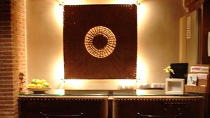 A bar area with two metal barstools, a circular wall decoration, and a small table with a lamp and a vase of flowers. - Rusticae Rincón de Traspalacio (Robledo de Chavela)