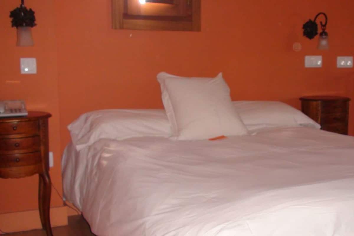 A bedroom with a large bed, two bedside tables, and a wall-mounted lamp.