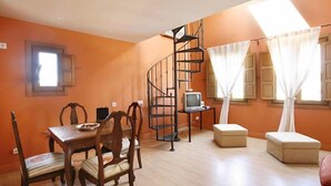 A room with a dining table, chairs, a TV, a staircase, and a window with curtains. - Rusticae Rincón de Traspalacio (Robledo de Chavela)