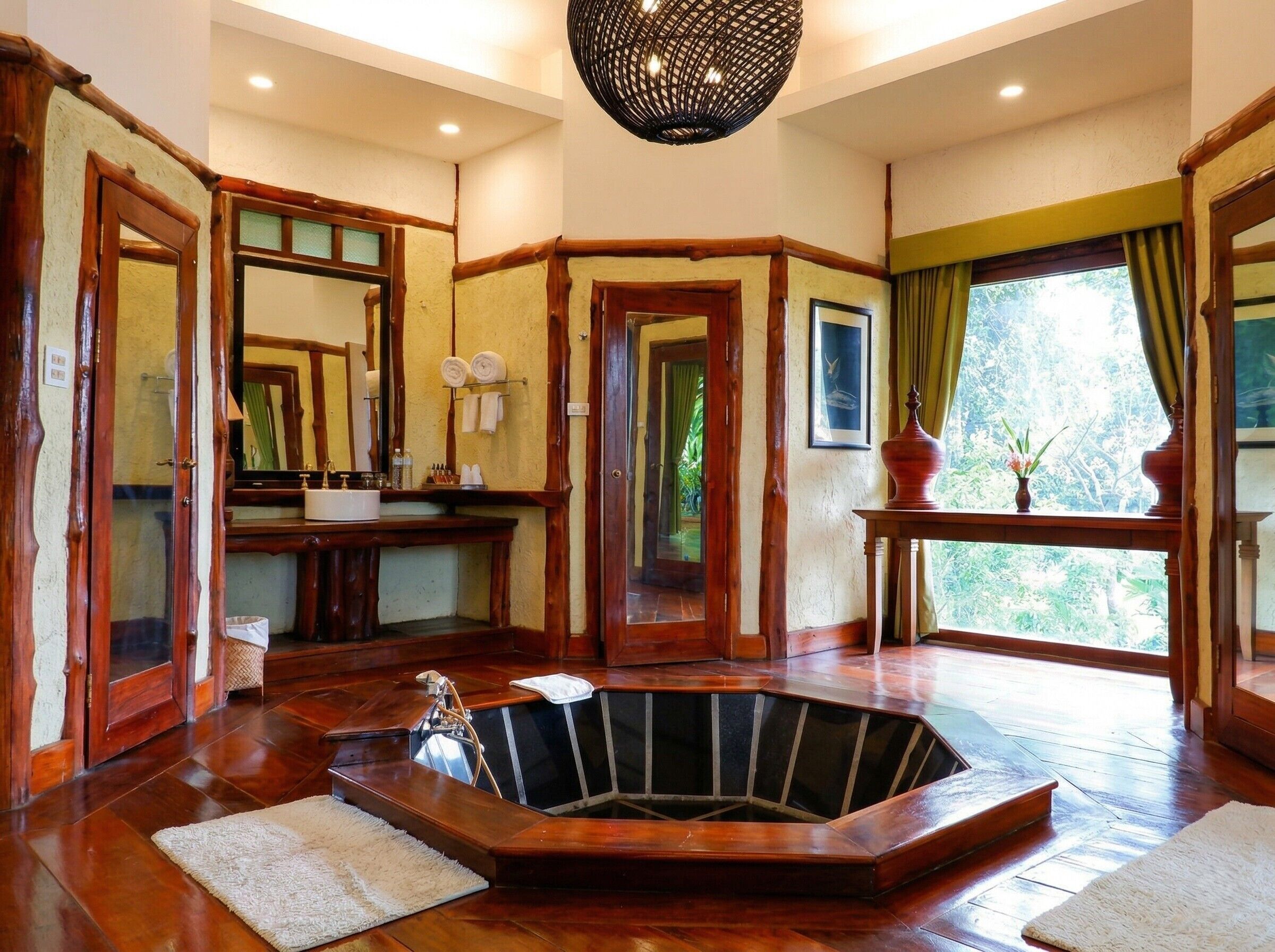 A spacious bathroom with a large bathtub, wooden accents, a mirror, and a view of greenery.