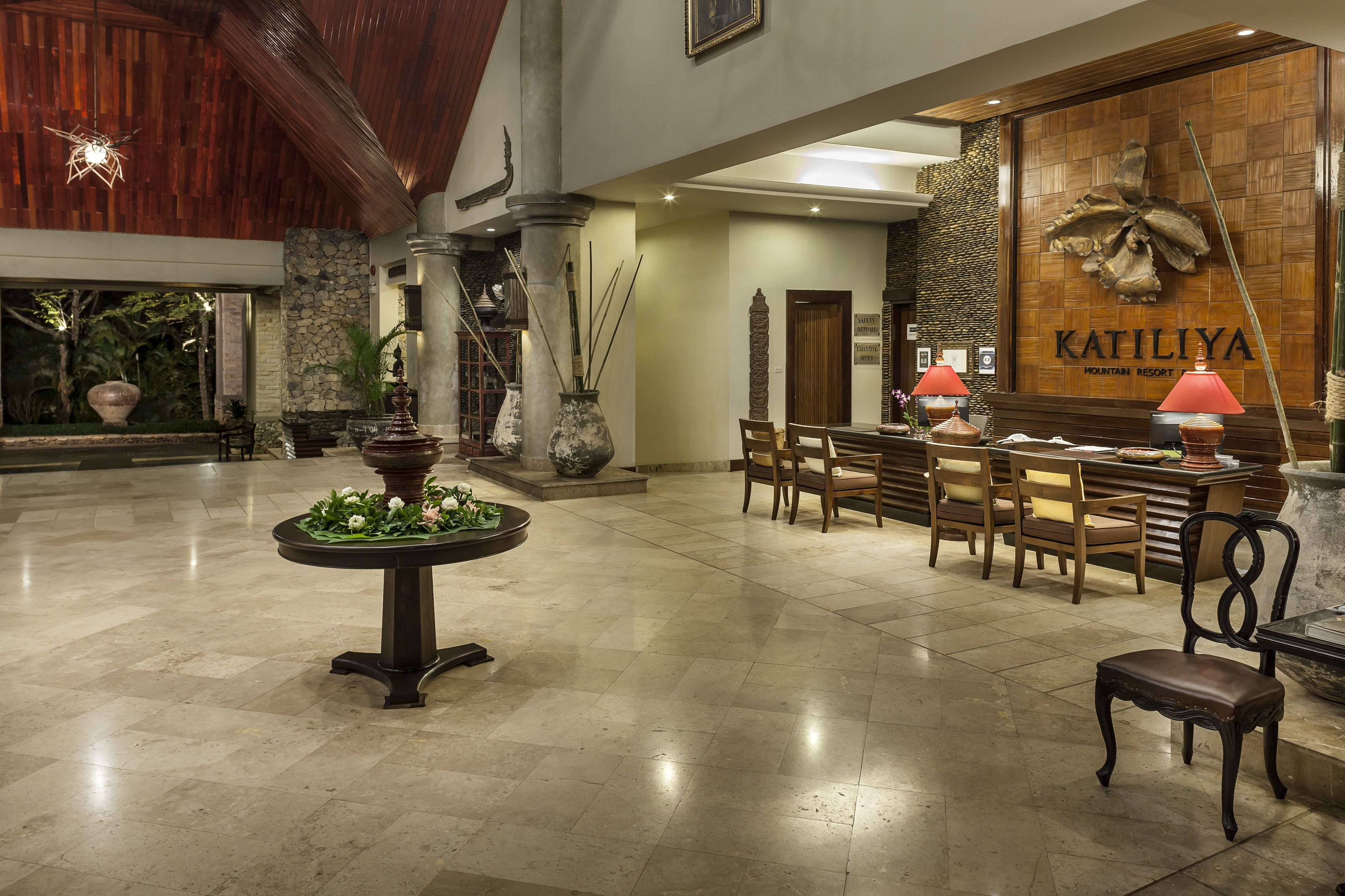 A spacious lobby with a reception desk, wooden chairs, a table with a vase of flowers, and a large wall with the name 'KATILIYA'.