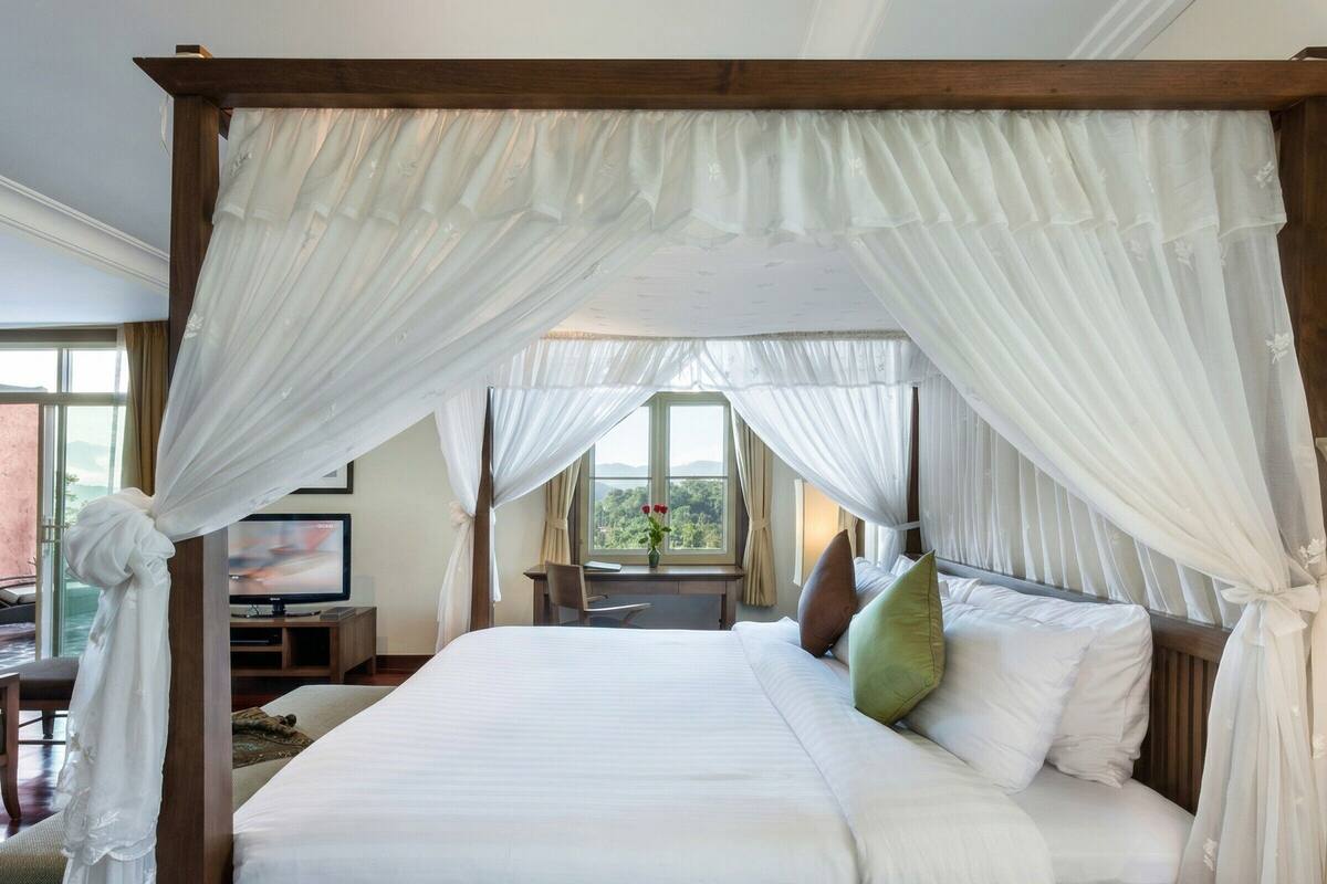 A four-poster canopy bed with a view of greenery outside.