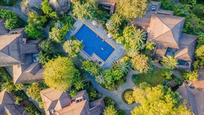 Luchtbeeld van een resort met meerdere bungalowachtige gebouwen, een centraal zwembad en omringende weelderige begroeiing.