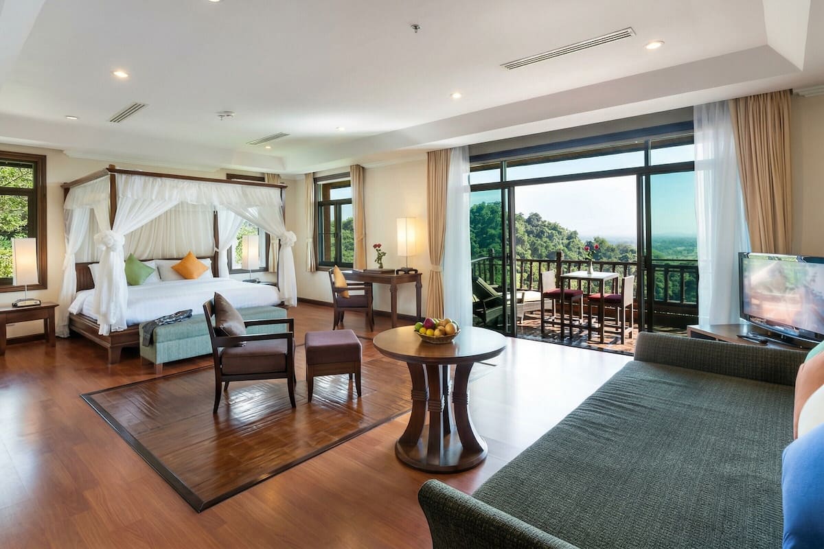 A hotel room with a four-poster bed, a balcony with a table and chairs, and a television.