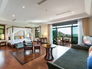 Una habitación de hotel con cama con dosel, un balcón con mesa y sillas, y un televisor.