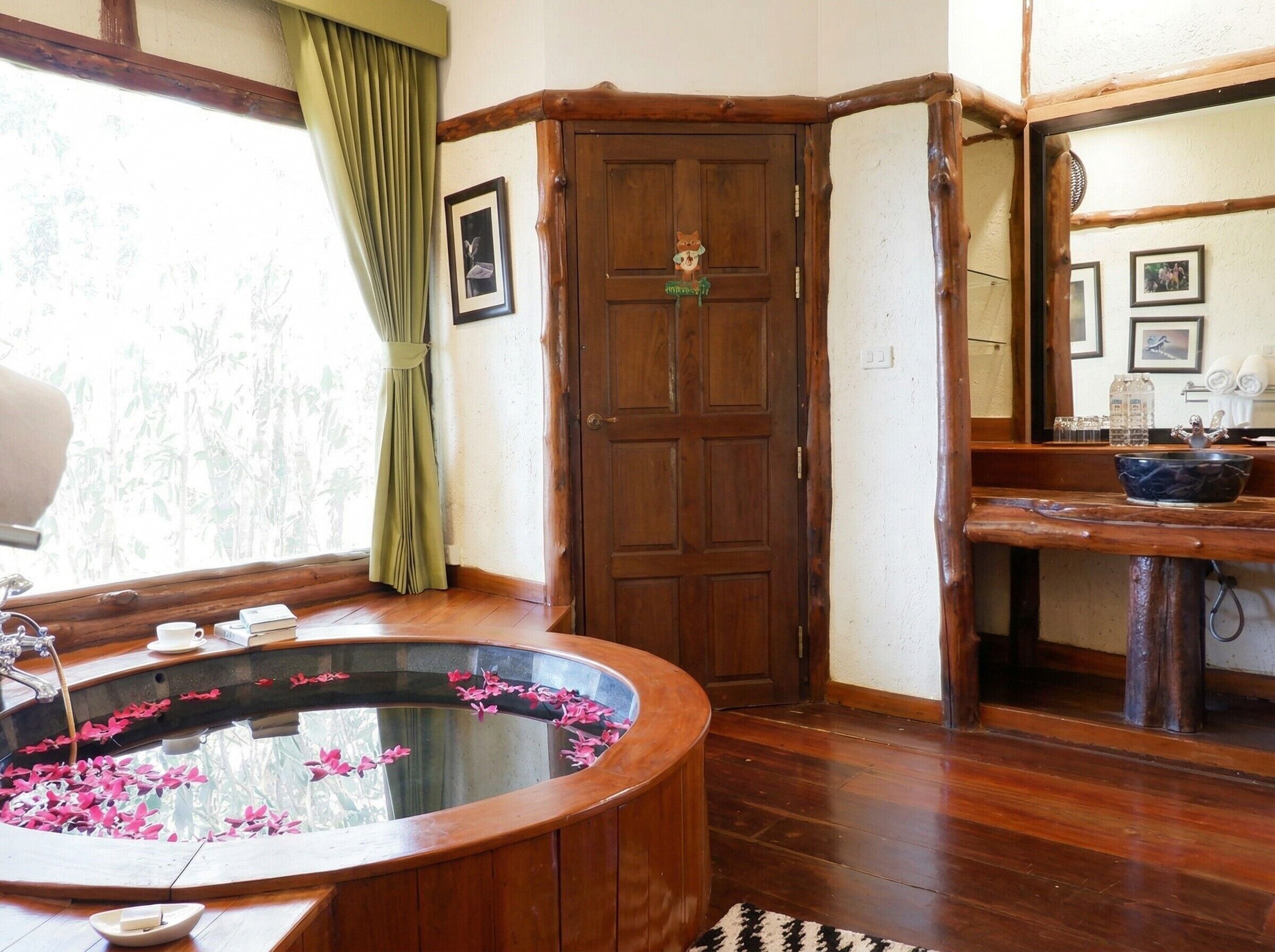 A bathroom with a wooden bathtub, a mirror, a sink, and a window with curtains.