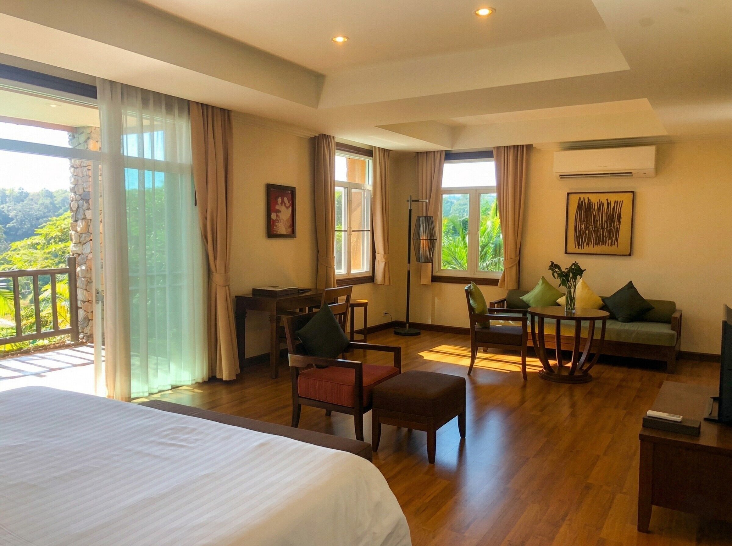 Une chambre d’hôtel équipée d’un lit, d’un bureau, d’une chaise, d’un canapé, d’une table et offrant une vue sur la verdure.