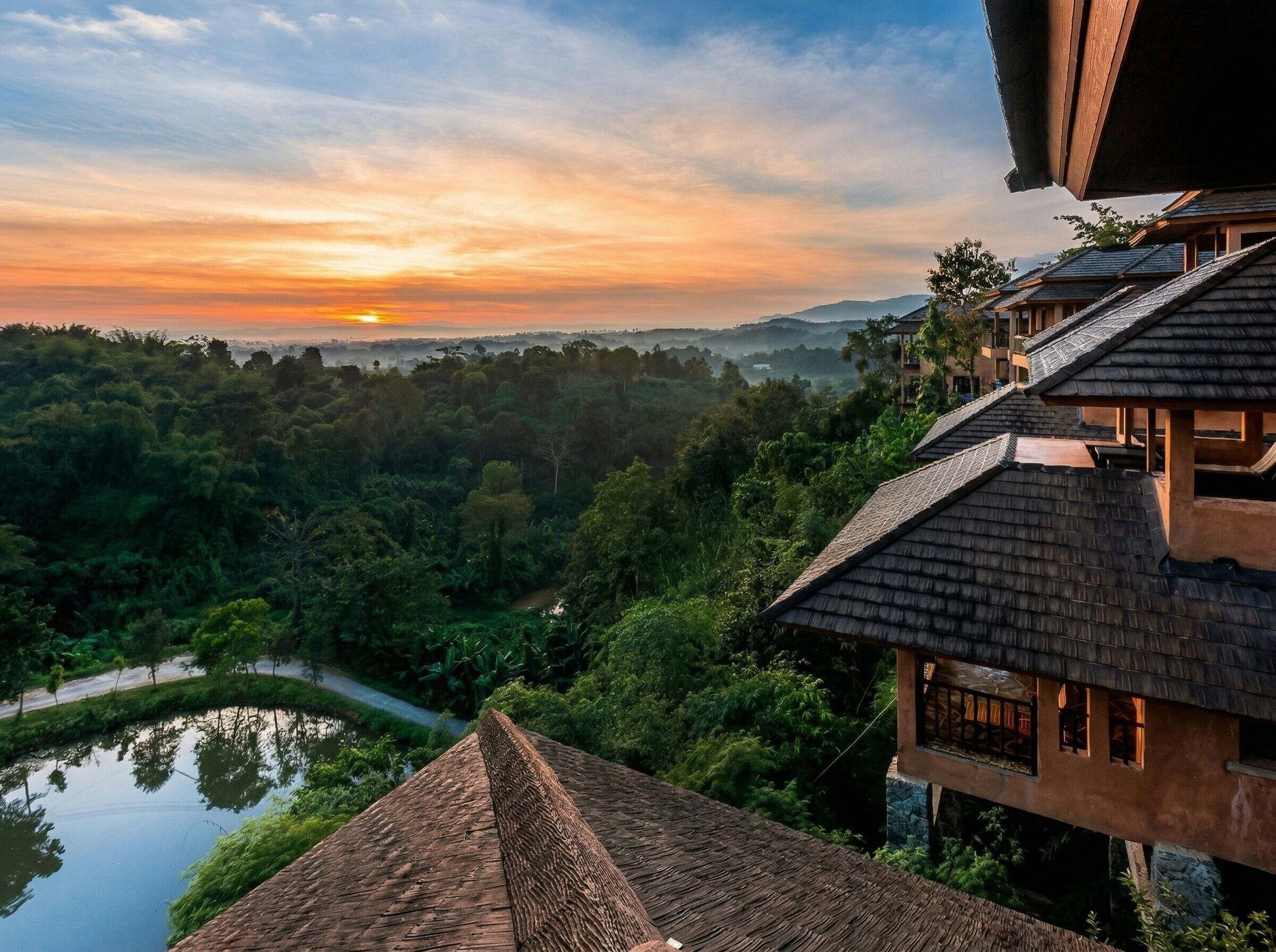 A traditional building with a steep roof, surrounded by lush greenery and a river.