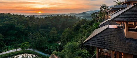 A traditional building with a steep roof, surrounded by lush greenery and a river.