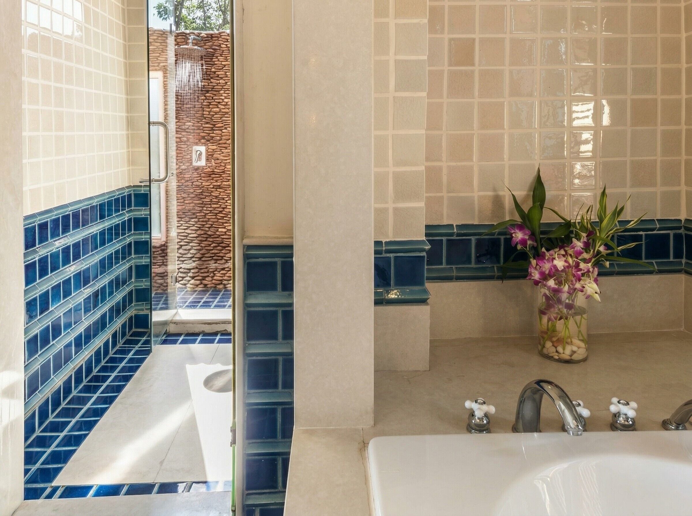 A bathroom with a bathtub, a shower, and a sink. There is a vase with flowers on the sink counter.