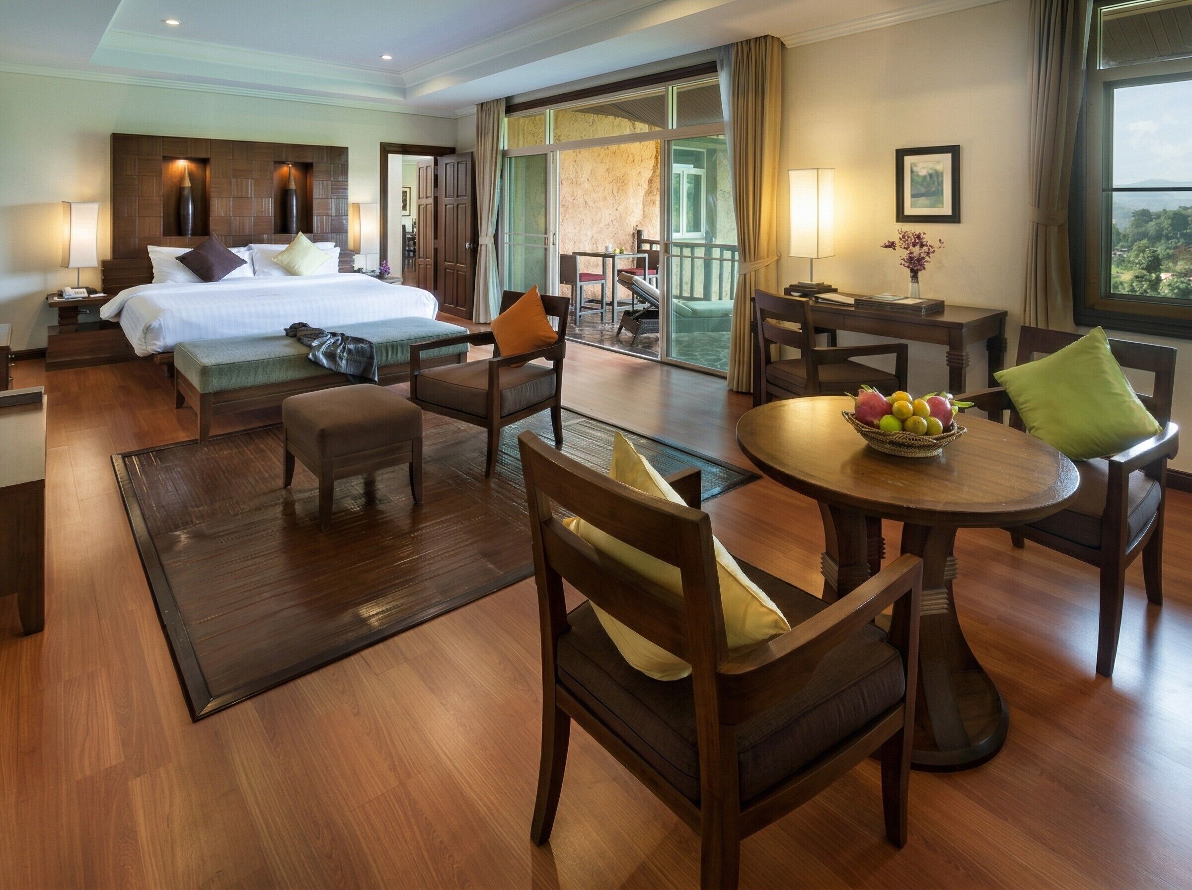 A hotel room with a bed, seating area, dining table, and a balcony with a view.