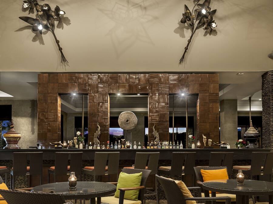 Een restaurant met ronde tafels en stoelen, een bar met een spiegel en decoratieve elementen, en hangende sterrenlampen.