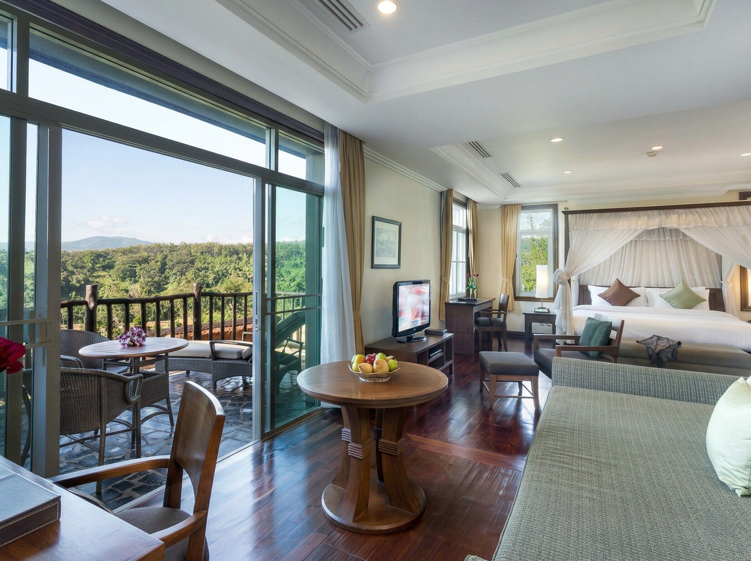 A hotel room with a balcony, a bed, a TV, a dining table, and a sofa.