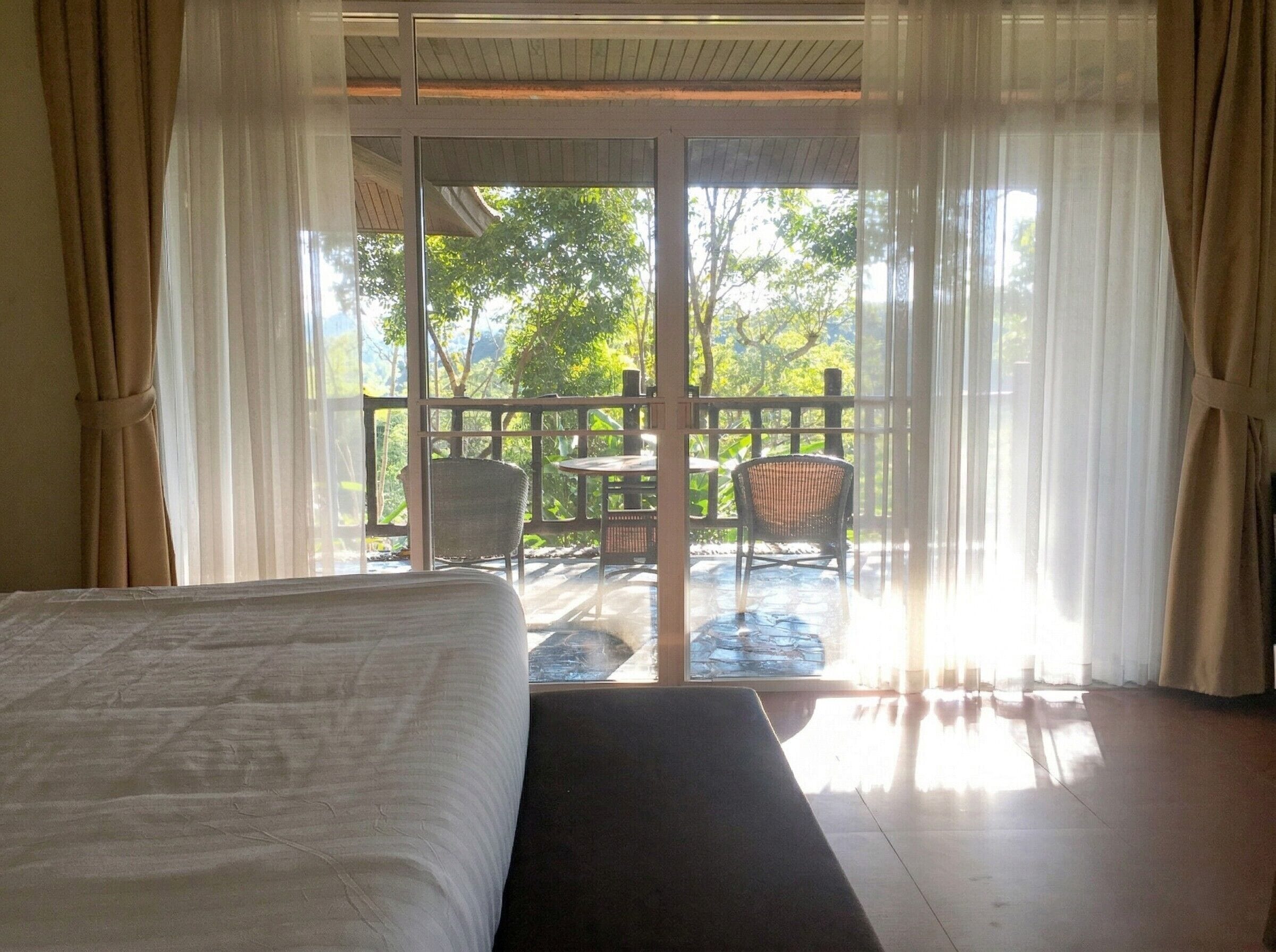 A room with a bed, a view of an outdoor deck with chairs and a table, and a sliding glass door.