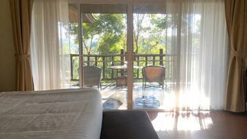 A room with a bed, a view of an outdoor deck with chairs and a table, and a sliding glass door.