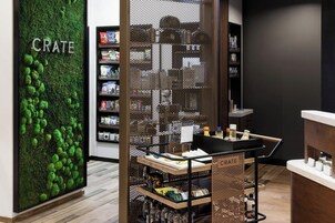 A modern retail store interior with a green moss wall labeled "CRATE," wooden shelves stocked with products, and a metal partition with "CRATE" signage.